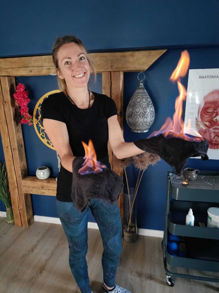 Chiński masaż ogniem Huo Liao masażysta trzymający w dłoniach płonące kompresy ziołowe nasączone alkocholem