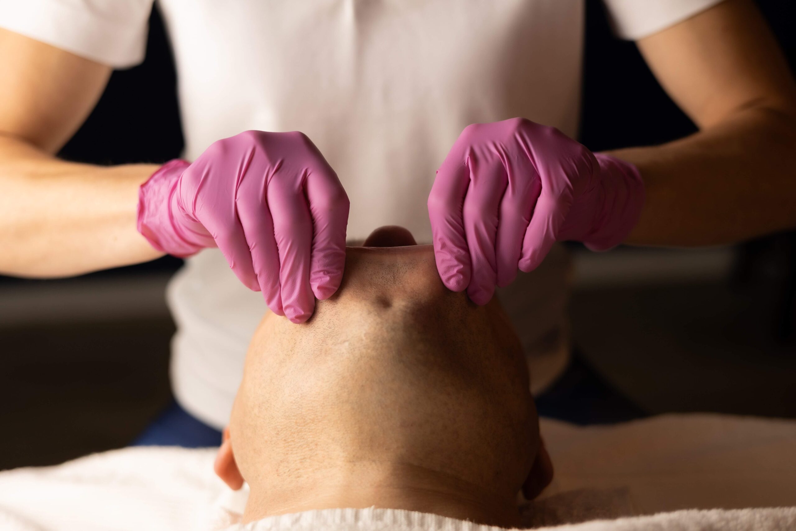 Specjalista wykonujący masaż transbukalny na twarzy pacjenta, koncentrując się na wewnętrznych i strukturach mięśnia okrężnego ust