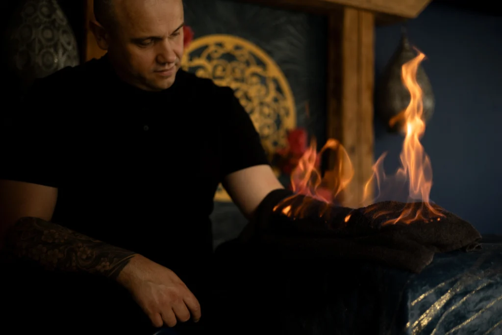 Instruktor masażu wykonujący masaż ogniem, z płomieniami na ręczniku, symbolizujący intensywne i holistyczne techniki masażu oferowane w Akademii Oriental SPA.
