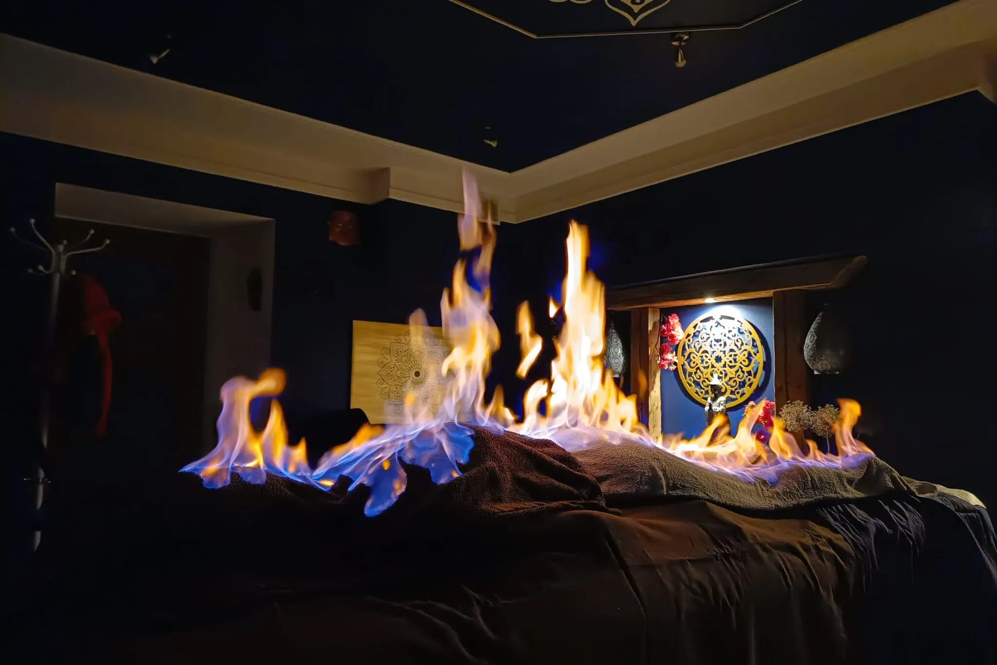 Tybetański Masaż Ogniem w gabinecie Akademii Oriental Spa – klient leży na stole do masażu przykryty warstwą ochronną, nad którą płoną kontrolowane płomienie; w tle orientalne dekoracje i mandala.